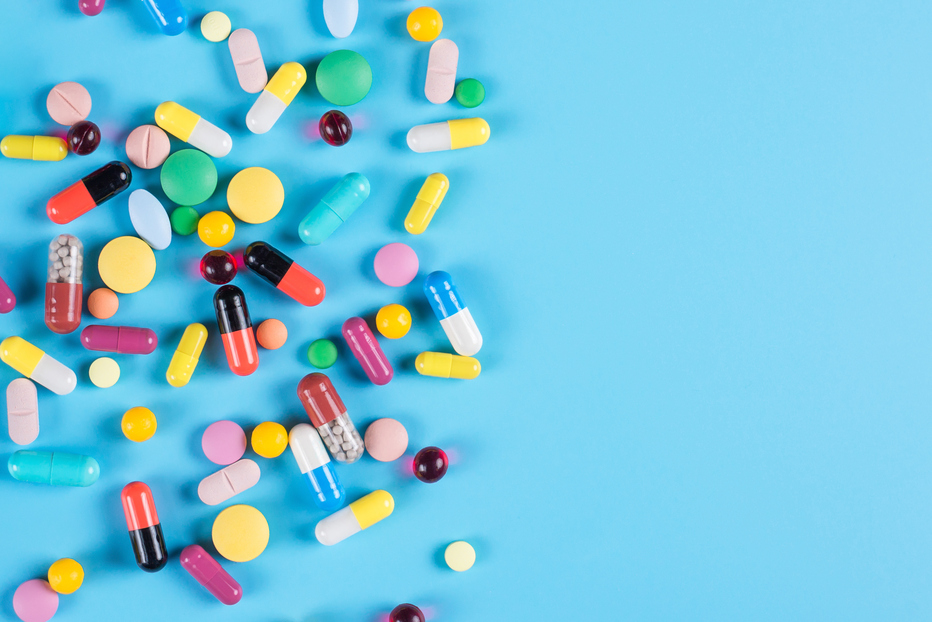 Medicine green, yellow, red and pink pills or capsules on a blue background with copy space.