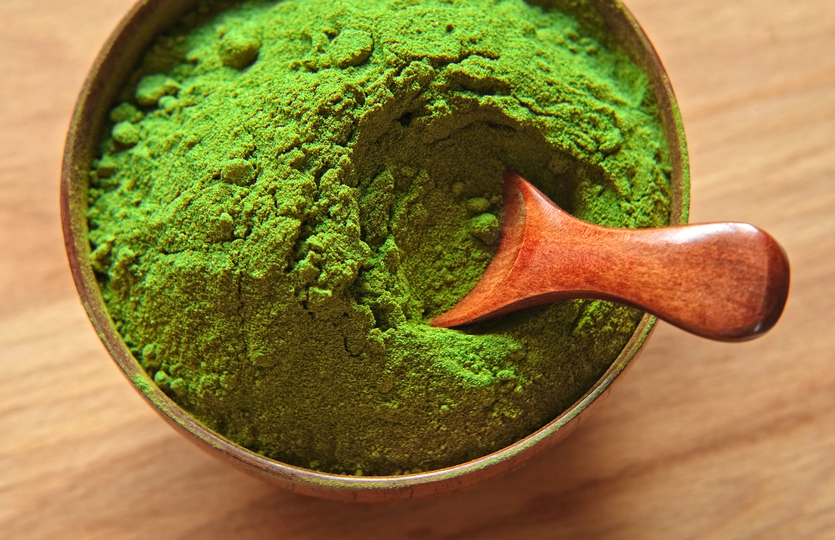 Wooden spoon with powdered matcha tea in a bowl spinning on natural background. Matcha powder. Top view, Closeup. Finely ground green powder. Japanese culture. Healthy eating with high antioxidants